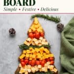 Christmas cheese board shaped like a tree with cubed cheddar, cherry tomatoes, and rosemary sprigs