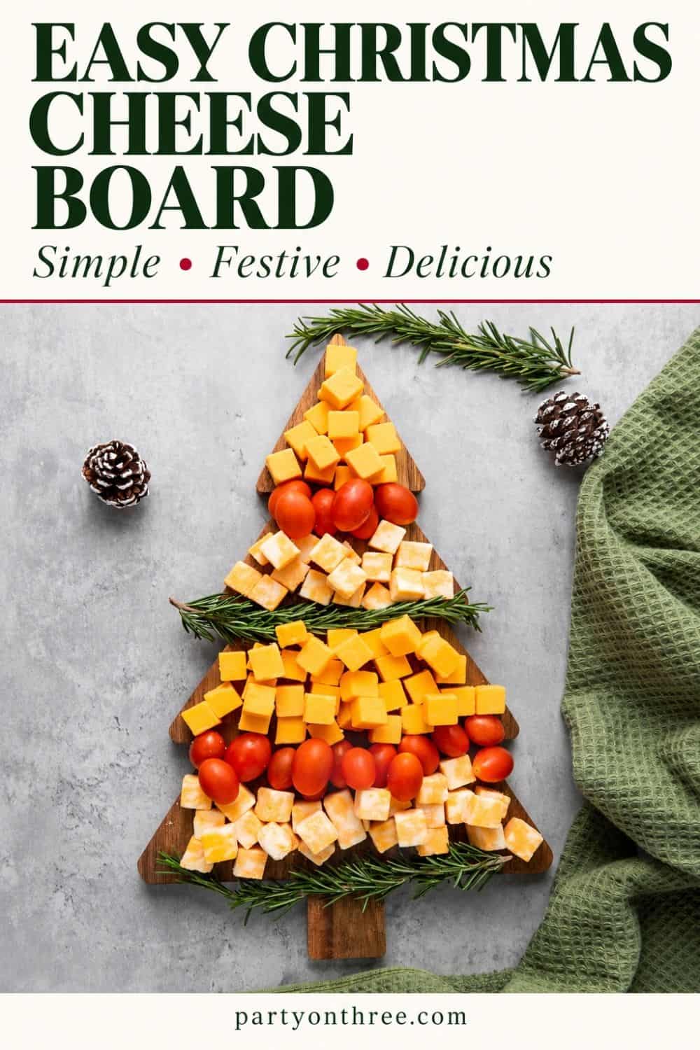 Christmas cheese board shaped like a tree with cubed cheddar, cherry tomatoes, and rosemary sprigs