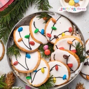 Christmas Light Cookies with white icing and candy "bulbs" piped with cord lines, arranged on a tin tray with greenery