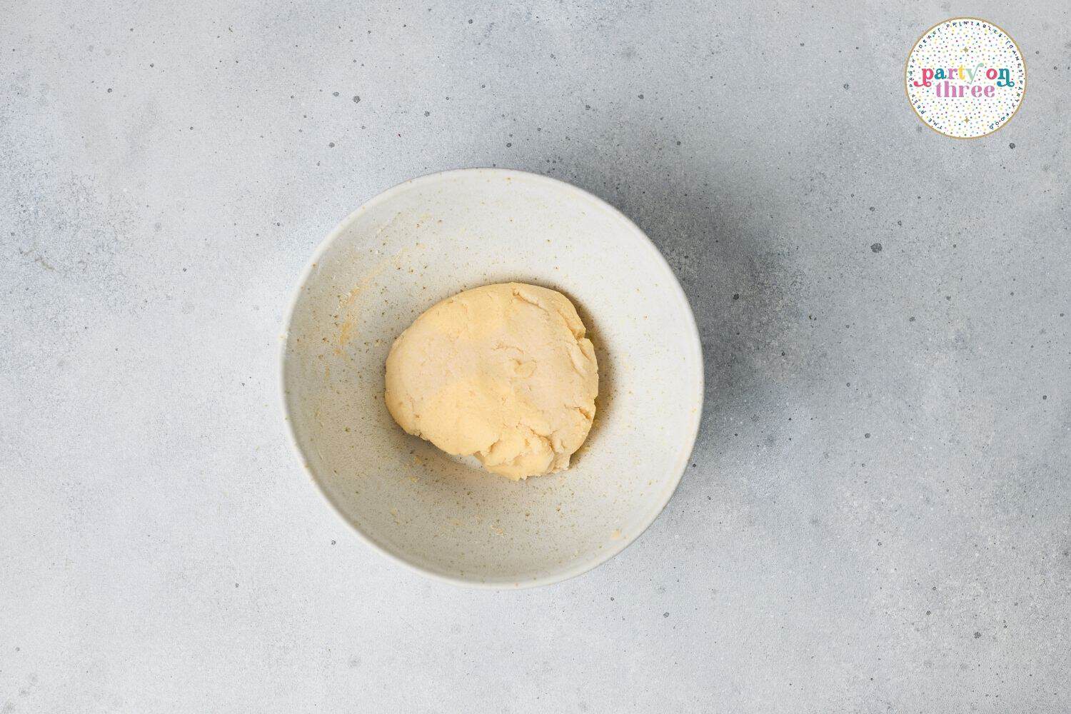 Ball of chilled sugar cookie dough resting in a white bowl, ready for rolling and cutting.