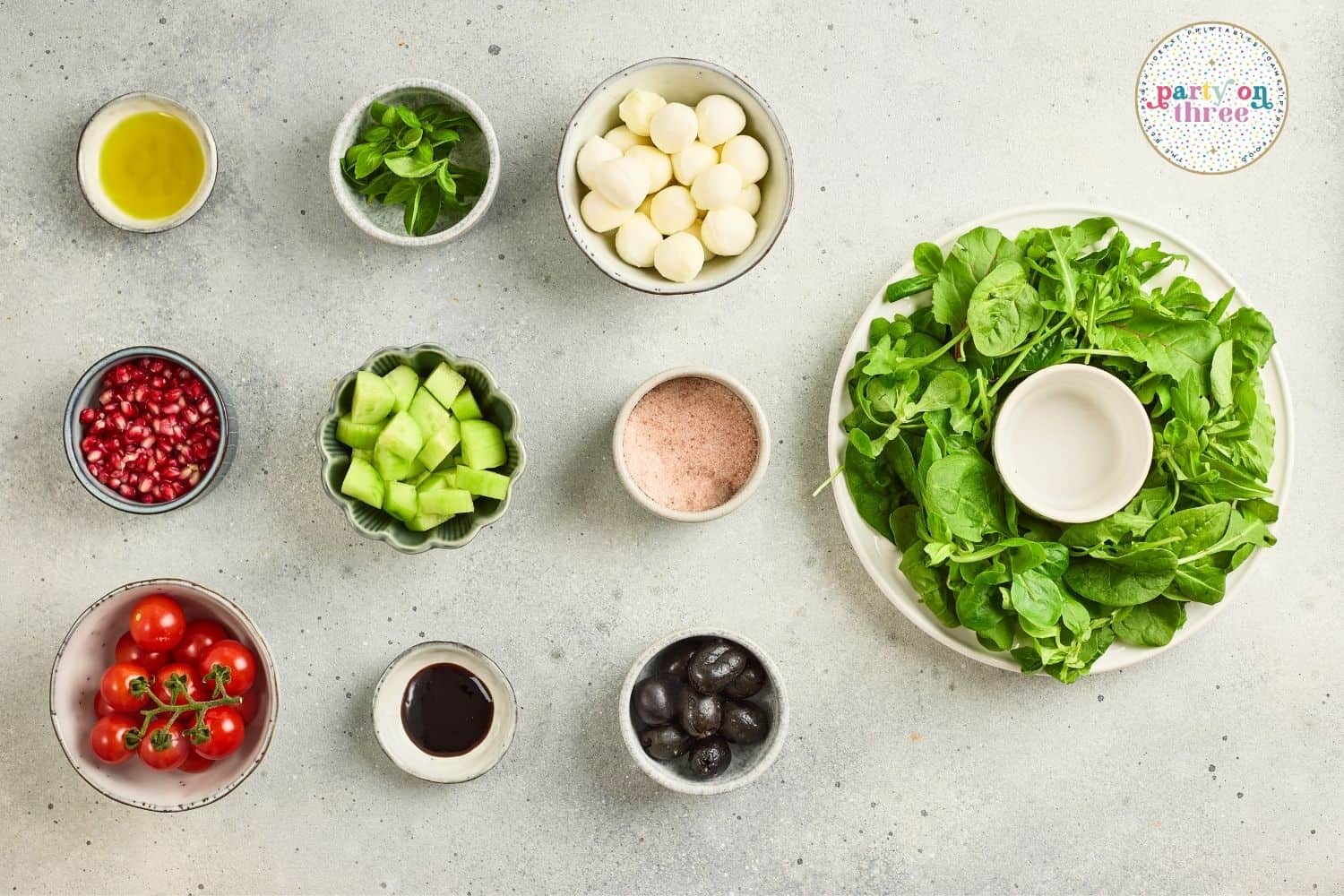 Ingredients for Christmas Wreath Salad: greens, mozzarella, tomatoes, cucumber, olives, pomegranate, mint, oil, vinegar, salt