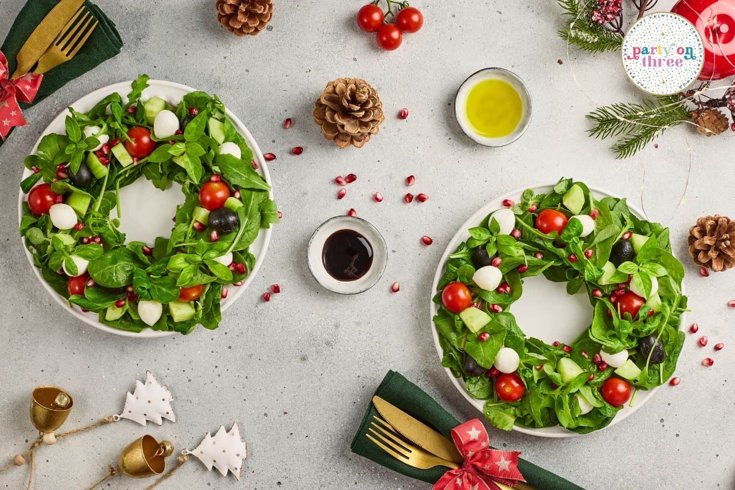 Two wreath-shaped salads with greens, tomatoes, mozzarella, cucumber, and pomegranate seeds on white plates