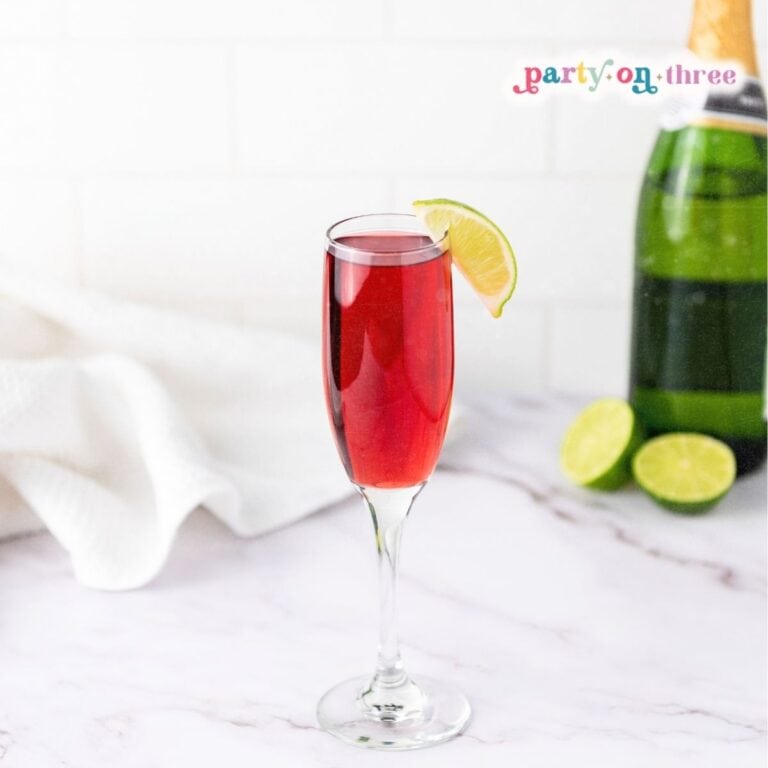 Cranberry mimosa in a champagne flute with a lime wedge garnish, next to a sparkling wine bottle.