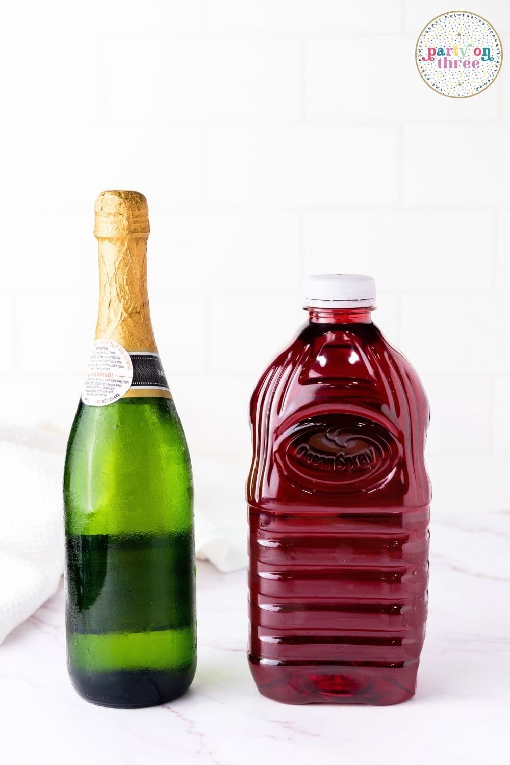 Bottle of champagne next to a bottle of cranberry juice, the ingredients for cranberry mimosas