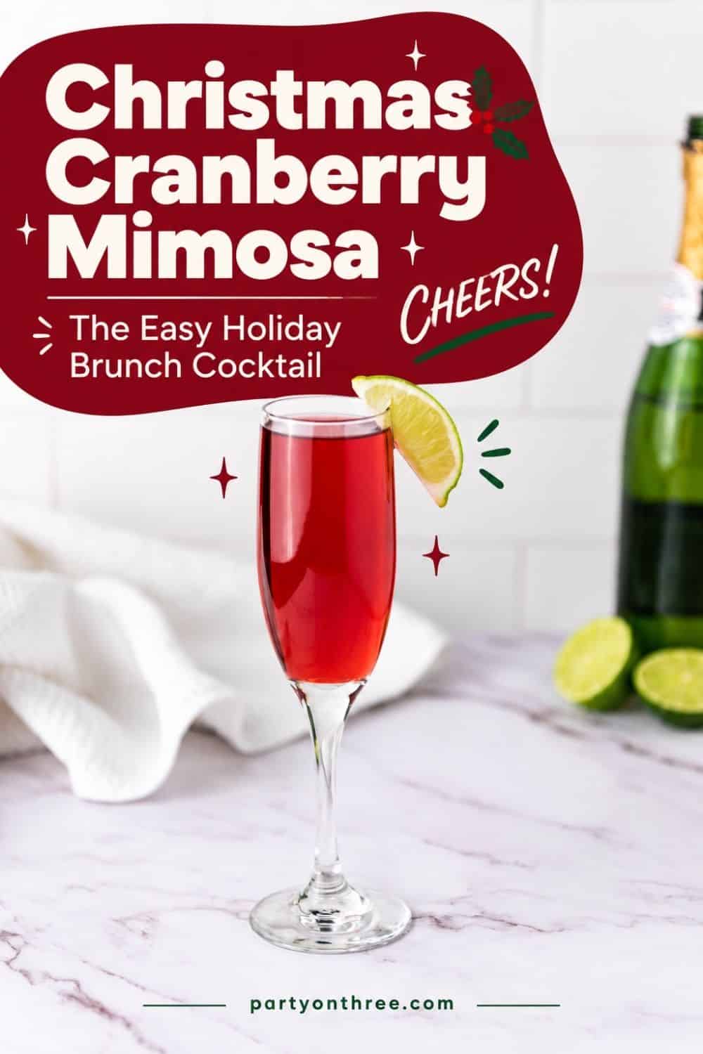 Cranberry Mimosa in a champagne flute with a lime wedge garnish, next to a bottle of champagne