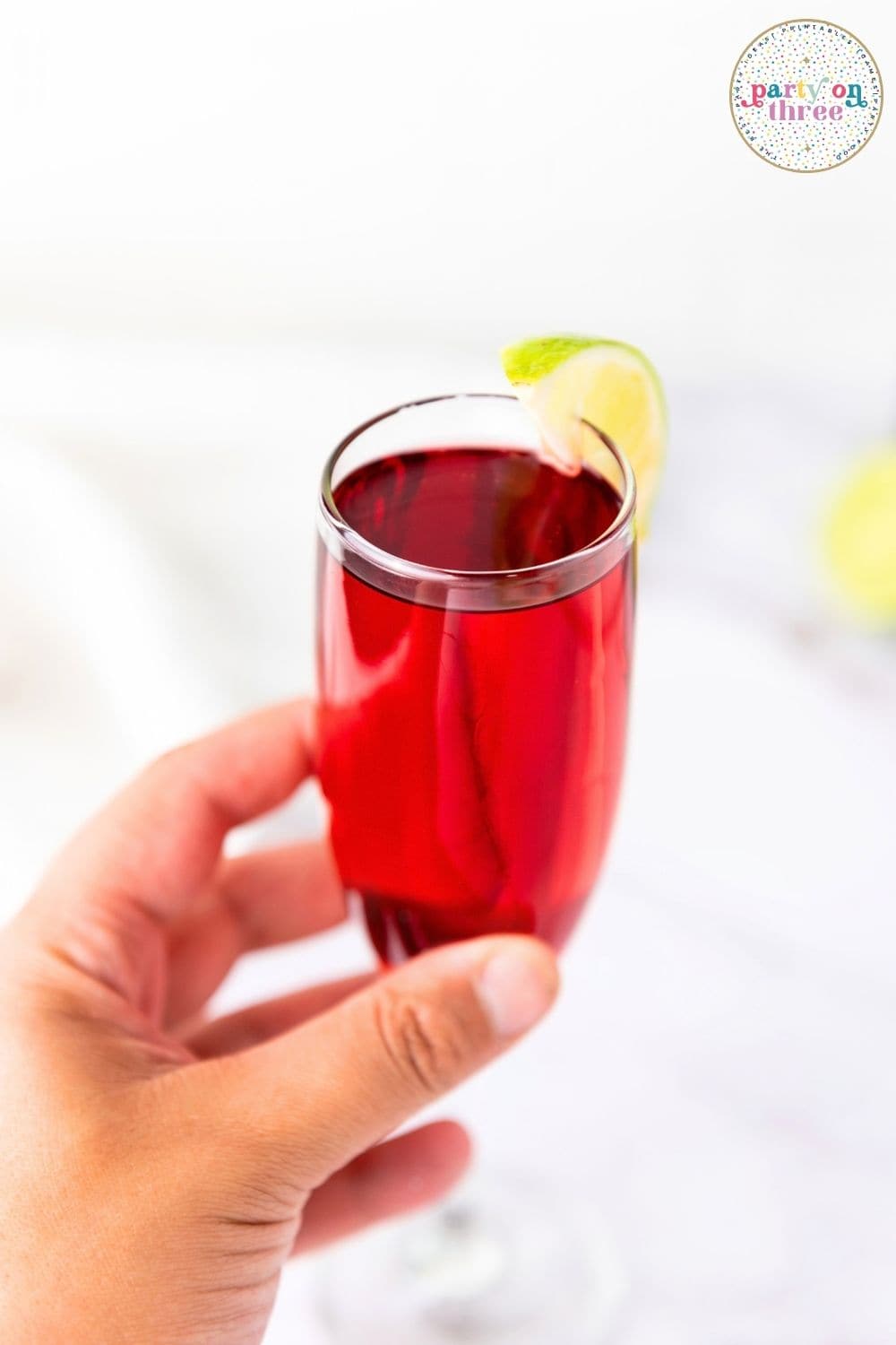 Hand holding a champagne flute filled with red cranberry mimosa, garnished with a lime wedge.