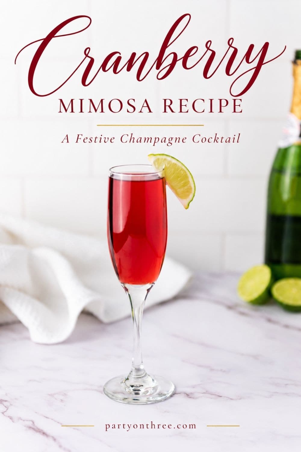 Cranberry mimosa in a champagne flute garnished with a lime wedge, next to a bottle of champagne and limes