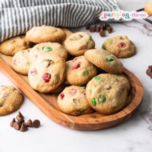 Easy Christmas cookies with red and green M&Ms on a wooden tray, with chocolate chips scattered nearby
