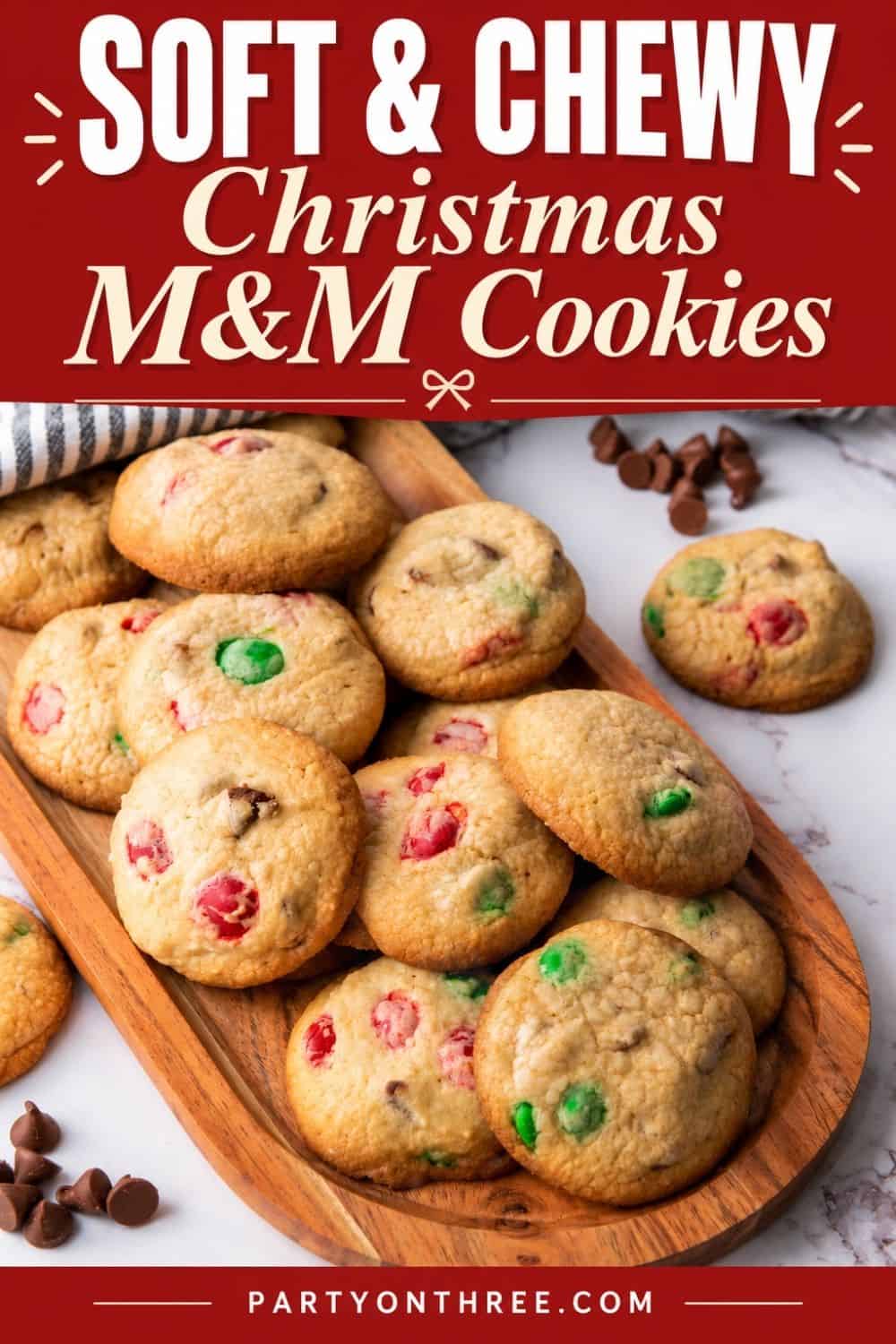 Easy Christmas cookies with red and green M&Ms piled on a wooden board, chocolate chips scattered nearby.