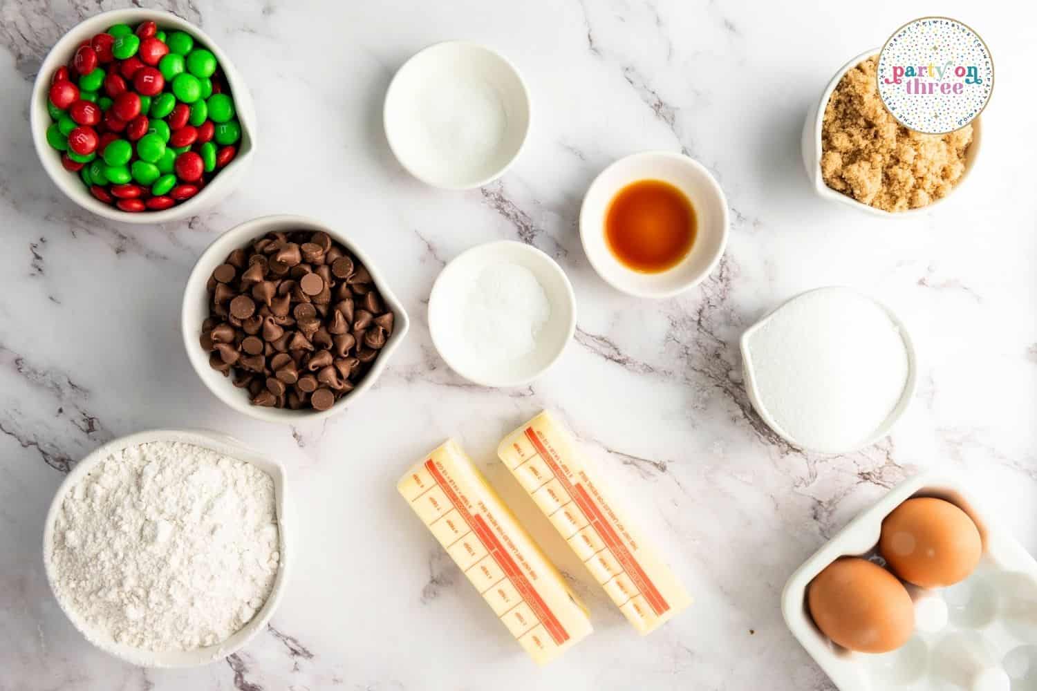 Ingredients for easy Christmas cookies: red and green M&Ms, chocolate chips, butter, flour, sugar, eggs, vanilla
