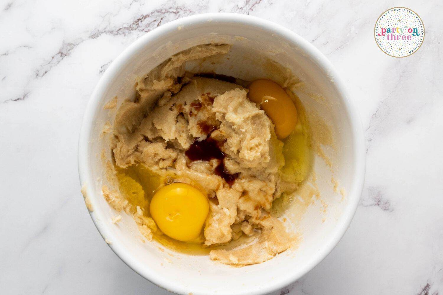 Eggs and vanilla extract added to creamed butter and sugar mixture in a white mixing bowl