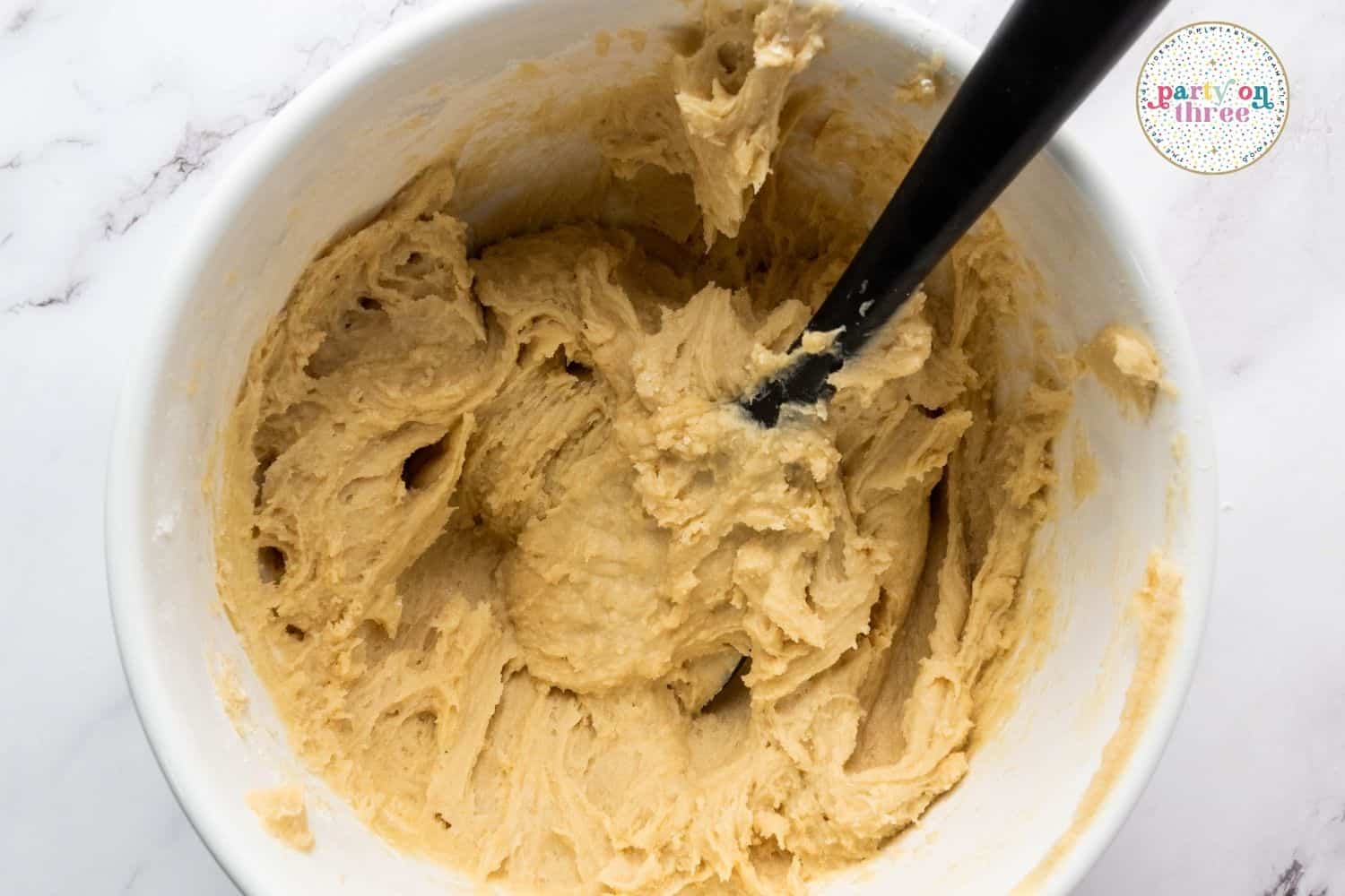 Creamed butter and sugar mixture in a white bowl, pale and fluffy, with mixer attachment inside
