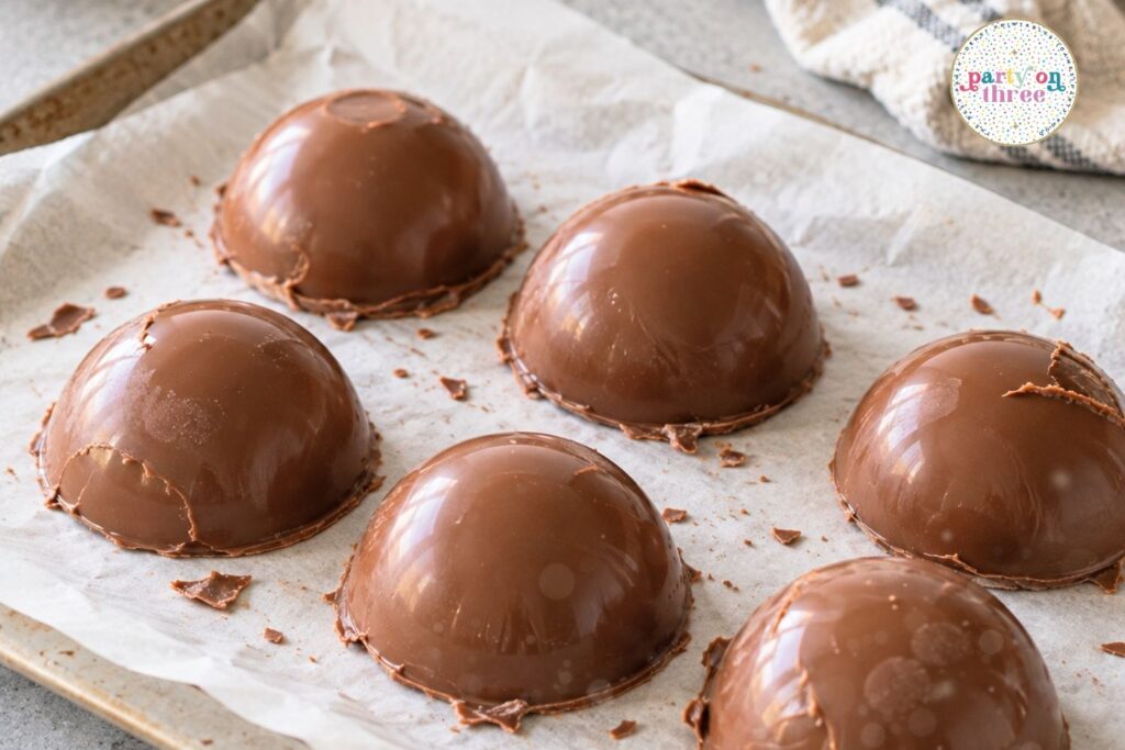 Six hollow chocolate half-sphere shells on parchment paper.