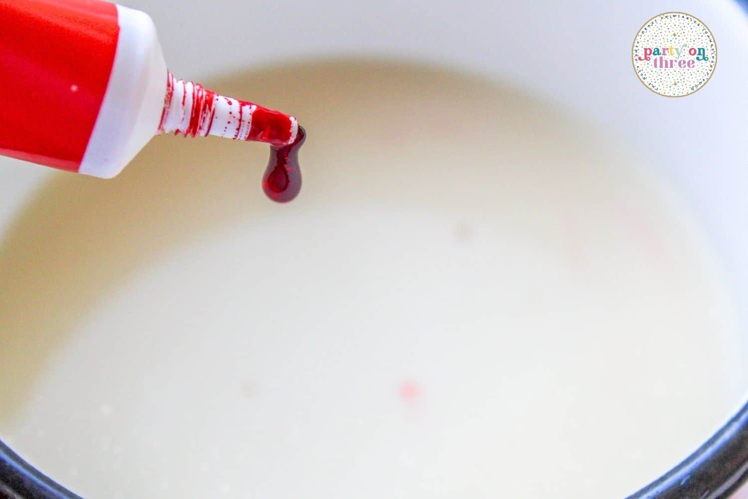A drop of red gel food coloring falling into a saucepan of milk