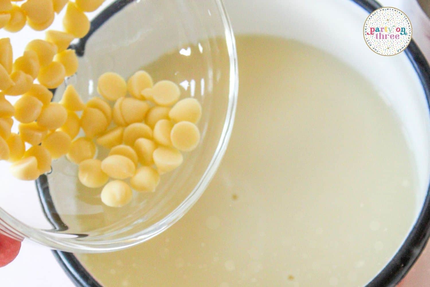 White chocolate chips being poured into a saucepan of warm milk