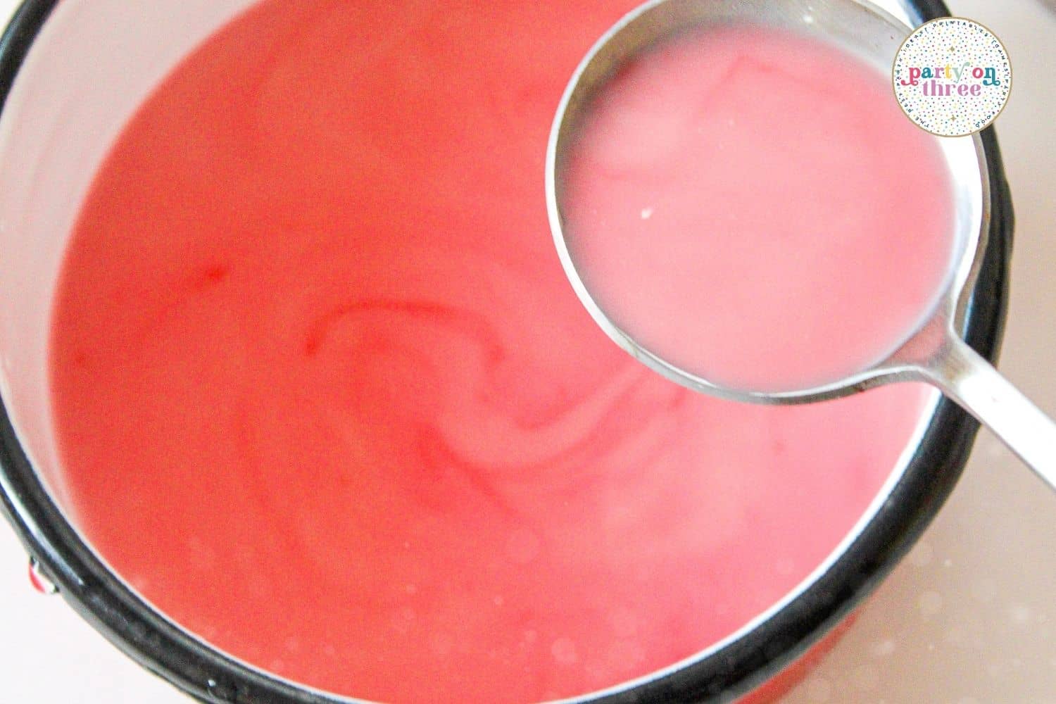 A ladle stirring pink hot chocolate in a saucepan until the white chocolate melts