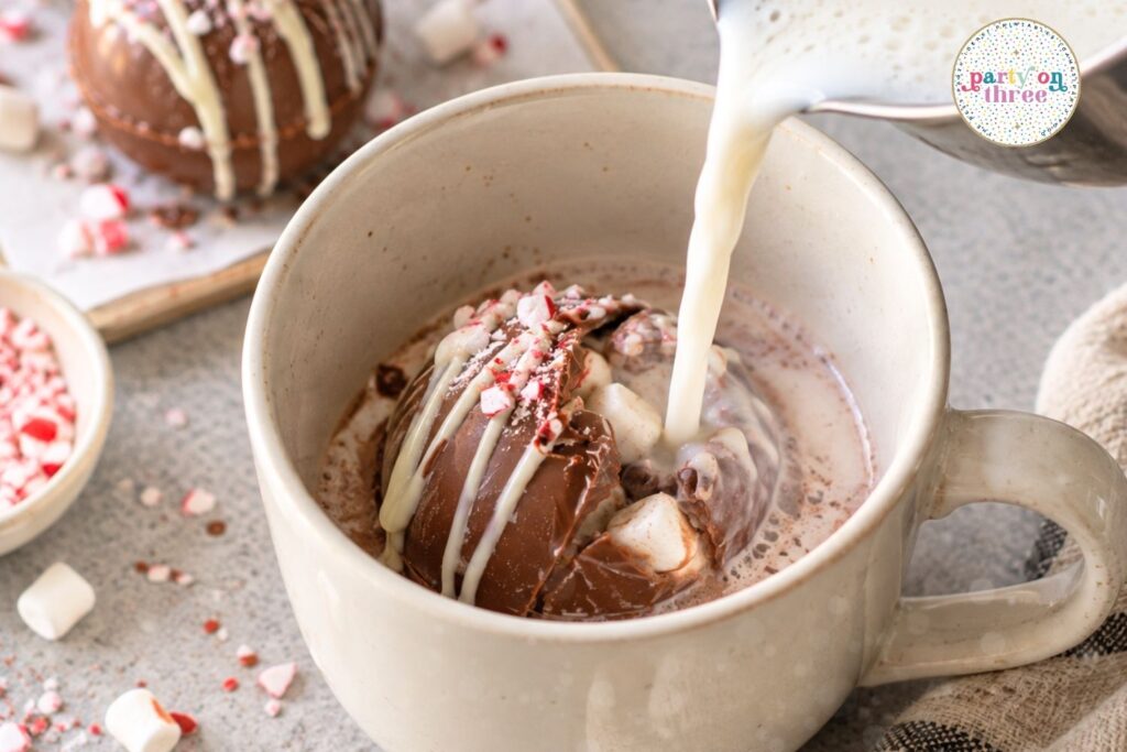 Pouring hot milk over a hot chocolate bomb in a mug