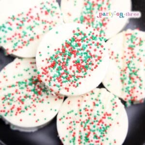 White chocolate-coated Ritz Cracker Christmas cookies topped with red, green, and white sprinkles on a black plate