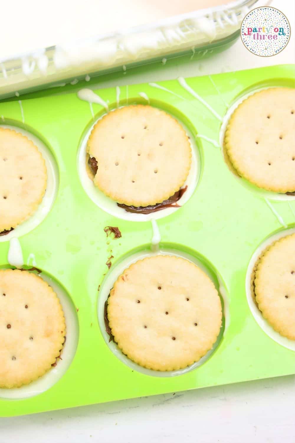 Ritz crackers topped with Nutella sitting in a green silicone mold, white chocolate coating edges of cavities.