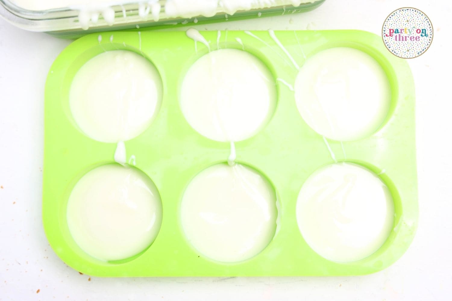 Melted white chocolate filling round cavities of a green silicone mold for dipping cookies