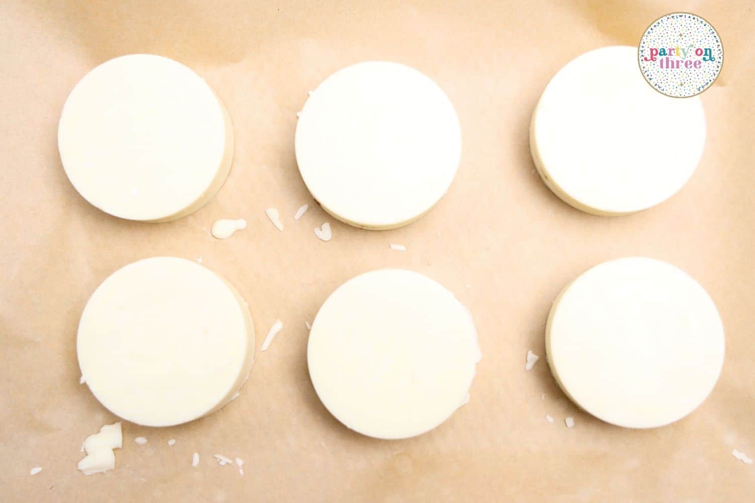 Six white chocolate-coated Ritz cracker sandwiches set on parchment paper before decorating