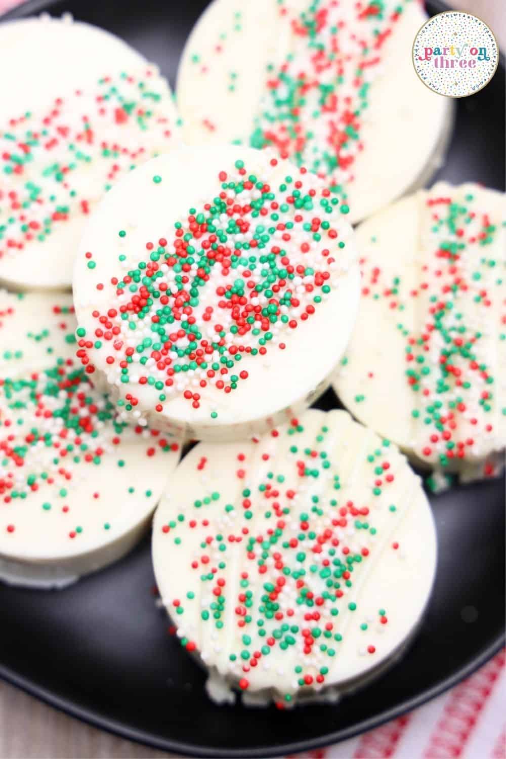 White chocolate-dipped Ritz Cracker Christmas cookies topped with red and green sprinkles on a black plate